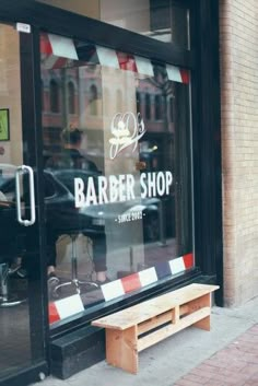 a barber shop with a wooden bench in front of the store's glass window