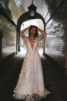 a woman in a long white dress standing in an archway with her hands on her head