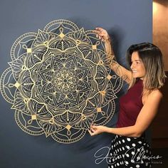 a woman is holding up a wall art piece with gold paint and intricate designs on it