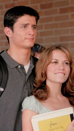 a man and woman standing next to each other holding an award in front of a brick wall