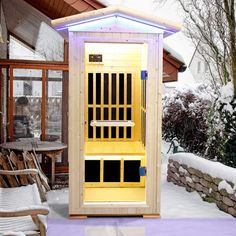 an outdoor sauna in the snow next to a chair and table with two chairs