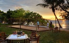 two people are standing on the deck overlooking the water at sunset or sunrise, with chairs and tables set out for dinner