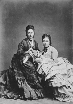 an old black and white photo of two women in formal dress sitting next to each other