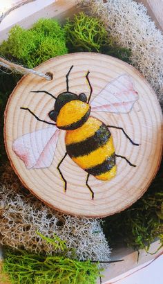 a bee painted on a piece of wood sitting in some mossy grass and dirt