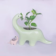 a planter shaped like an elephant is next to a small toy dinosaur with a green plant in it