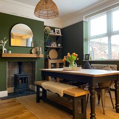 a dining room with green walls and wood flooring has a bench in front of the fireplace