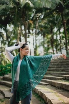 a woman wearing a green shawl standing in front of some steps with her arms outstretched