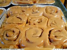 there are many rolls covered in caramel icing on top of tin foil trays