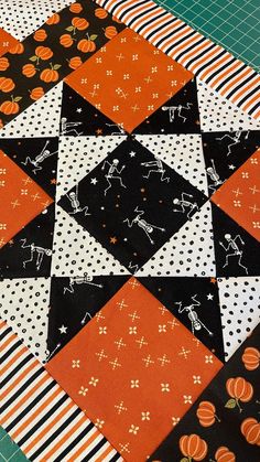 an orange, black and white patchwork quilt with pumpkins on the top is laying on a cutting board