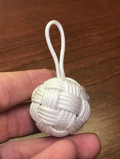 a hand holding a white ball ornament on a wooden table with a string attached to it