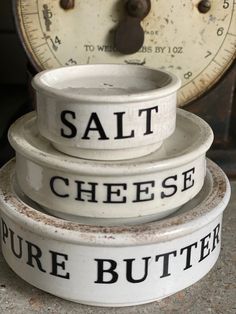 three white dishes stacked on top of each other in front of an old scale with the words salt cheese and pure butter