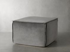 a square grey ottoman sitting on top of a gray floor next to a white wall