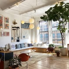 a living room filled with furniture and lots of windows next to a wooden floor covered in potted plants