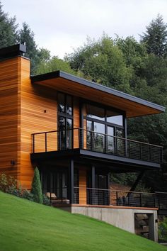 a modern house with wood siding and black balconies on the upper level, surrounded by lush green trees