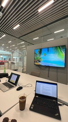 two laptops on a table in an office with a large screen tv above them