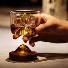 a hand holding a glass with some liquid in it and ice cubes on the rim