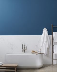 a white bath tub sitting next to a wooden bench in a bathroom with blue walls