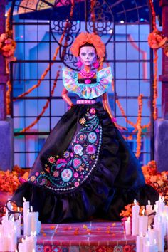 a woman in a black dress standing on a stage with candles and flowers around her