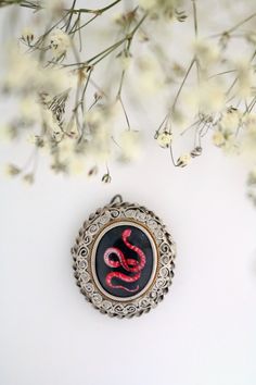 This pendant with hand painted miniature depicts one of the most fascinating and dangerous creatures on earth: the coral snake. Although he can kill in a few minutes, his appearance is decidedly colorful and elegant, so as to seem a sinuous jewel himself. The snake is an ancient symbol that can have both negative and positive meaning. Creature of evil and original sin in Genesis, it can also be synonymous with wisdom and infinity. The locket in which the miniature is inserted is antique in 800 s Vintage Silver Snake Jewelry, Vintage Snake-shaped Jewelry Gift, Vintage Snake Jewelry For Gifts, Snake-shaped Engraved Jewelry Gift, Victorian Silver Enamel Jewelry, Unique Engraved Snake Jewelry, Engraved Snake-shaped Jewelry Gift, Red Snake-shaped Jewelry For Gifts, Antique Hand Painted Jewelry For Gifts