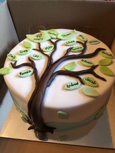 a white cake decorated with green and brown tree names on the side, sitting in a cardboard box