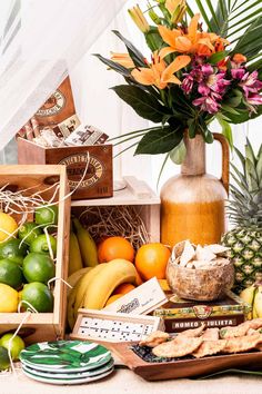 an assortment of fruits and vegetables on a table with a vase full of flowers in the background