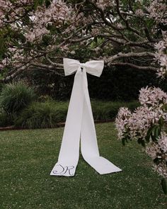 a white bow tied to the side of a tree in front of some bushes and flowers