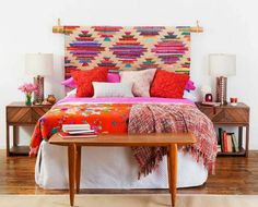 a bed with colorful blankets and pillows in a white room next to a wooden table