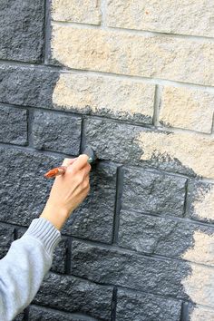 a person is painting the side of a brick wall with gray and white paint on it