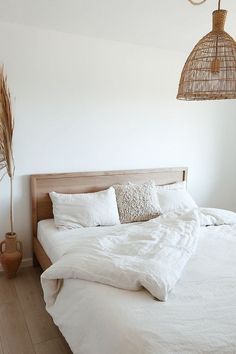 a bed with white linens and pillows in a bedroom next to a basket light