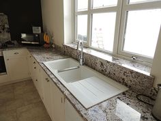 a kitchen with marble counter tops and white cabinets, along with a window over the sink