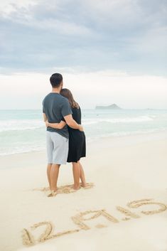 a man and woman standing on top of a sandy beach next to the word love written in the sand