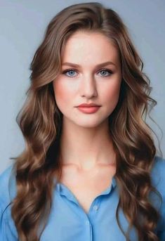 a woman with long hair and blue shirt posing for a photo in front of a gray background