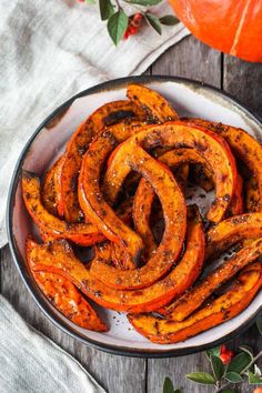 baked sweet potato wedges in a white bowl on a wooden table next to a pumpkin