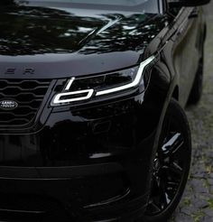 the front end of a black suv parked on a cobblestone road