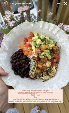 a person holding a plate with rice, beans and avocado on it in front of flowers