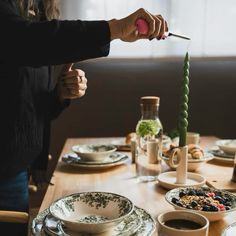 a woman cutting into a cake on top of a wooden table with plates and cups