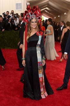 a woman in a black dress with red flowers on her head standing next to a man in a tuxedo