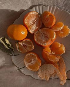 several oranges cut in half on a white plate with leaves and dried flowers next to them