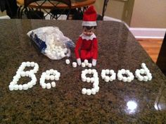 an elf sitting on top of a counter next to a bag of balls that say 3 o'clock