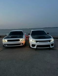 two white cars parked next to each other near the ocean at night with lights on