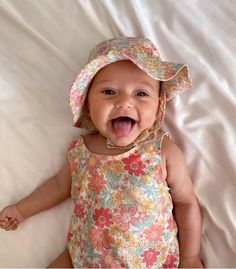 a baby laying on top of a bed wearing a hat and smiling at the camera