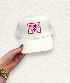 a person's hand holding up a white hat with the word alpha phi on it