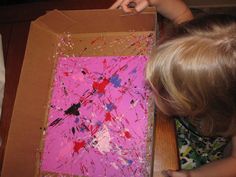 a child is painting on a box with pink paint