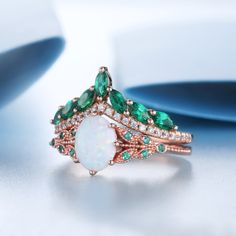 an opal and diamond ring with emeralds on the side, sitting on a white surface