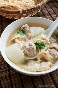 a bowl of soup with meatballs and dumplings in it next to a basket of bread