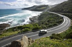 a white van driving down the side of a road next to the ocean on top of a hill