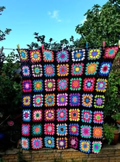 a crocheted blanket is hanging on a brick wall in front of some trees