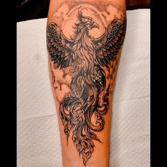 a woman's leg with an eagle tattoo on it and clouds in the background