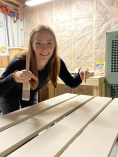 a woman is smiling and holding a paintbrush in front of some wood planks