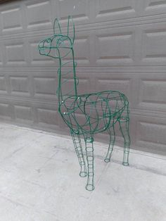 a green wire sculpture of a giraffe standing in front of a garage door